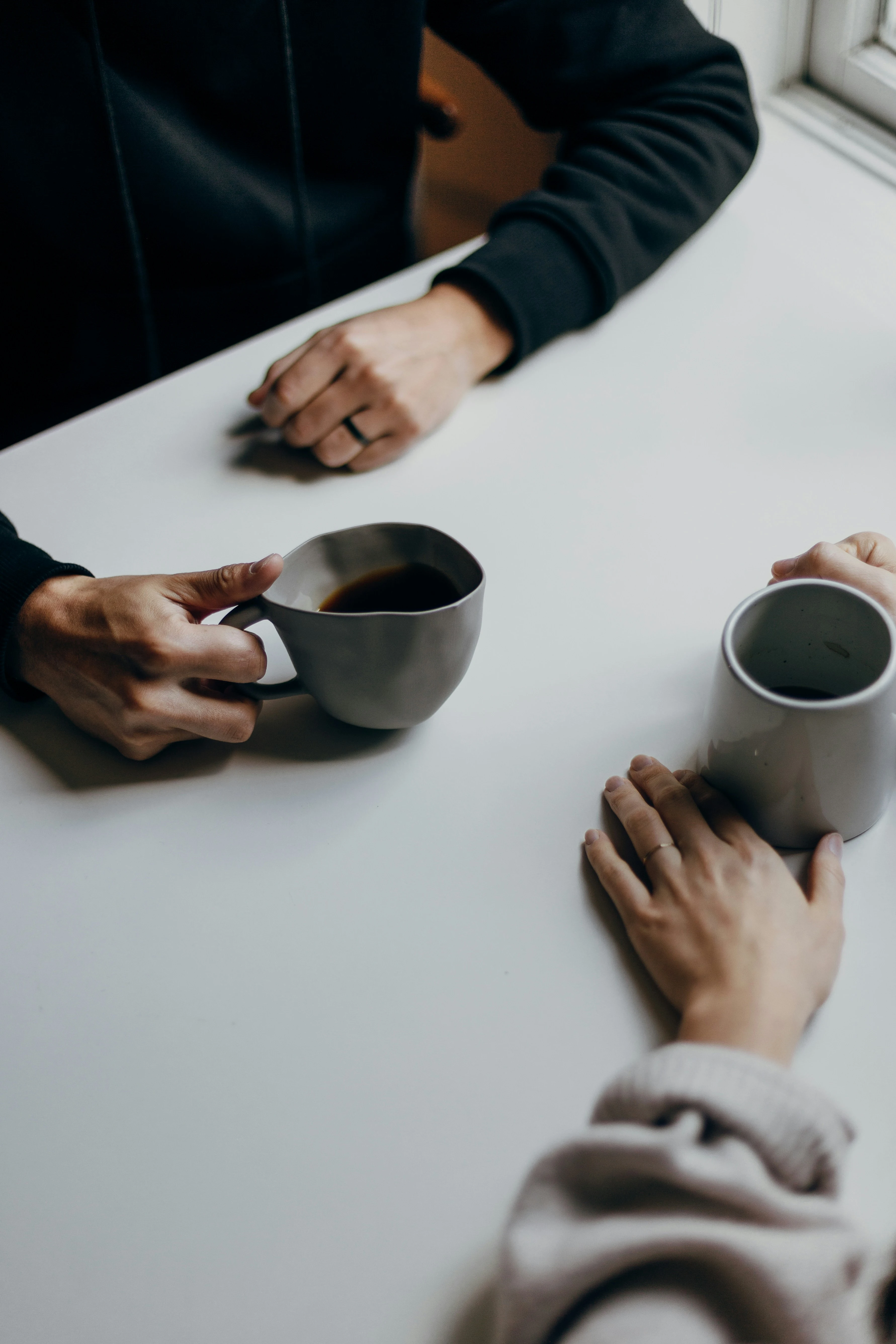An image of two sets people sitting at a table with coffee, just their arms and coffees are visible on a white table